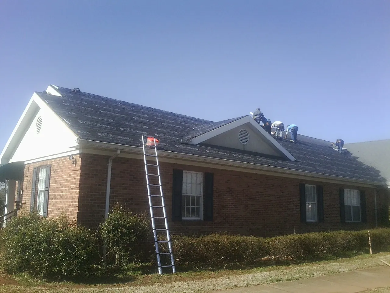 Crew tearing shingles off a brick ranch roof with a ladder set — Metal Roof Repair work by our crew in Waterville
