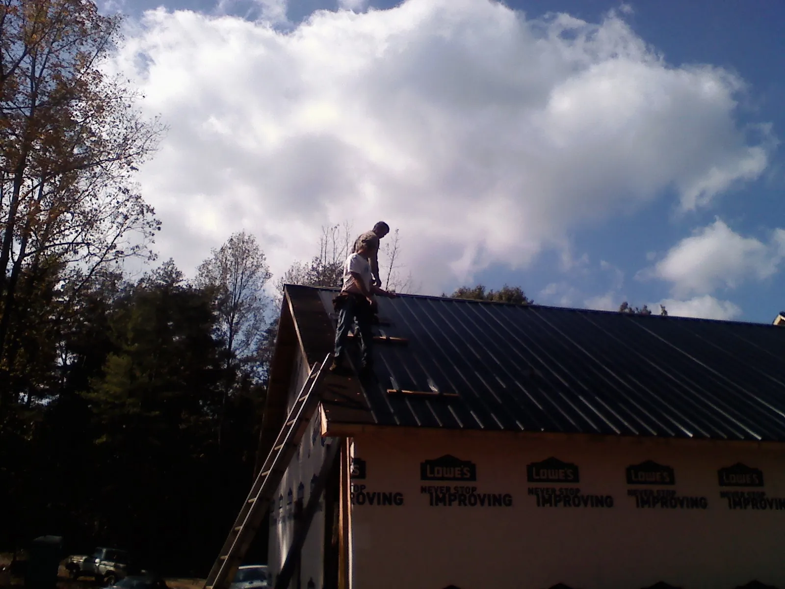 Roofer fastening dark metal panels high against a cloudy sky, from a Roof Inspection job in Waterville