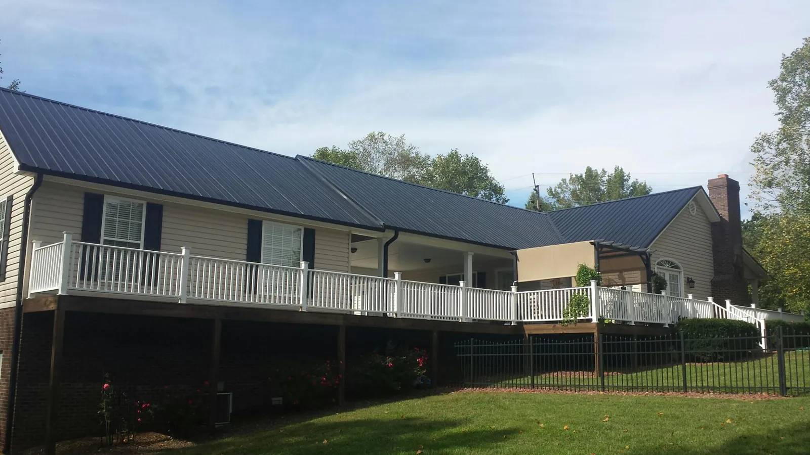 Black metal roof above a long white railed deck on a hillside home in Waterville